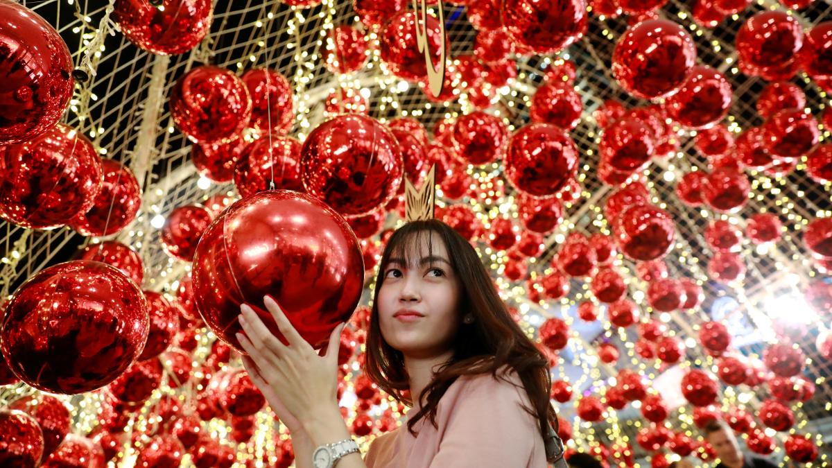 A woman poses for a photo surrounded by red Christmas ornaments in Bangkok, Thailand.