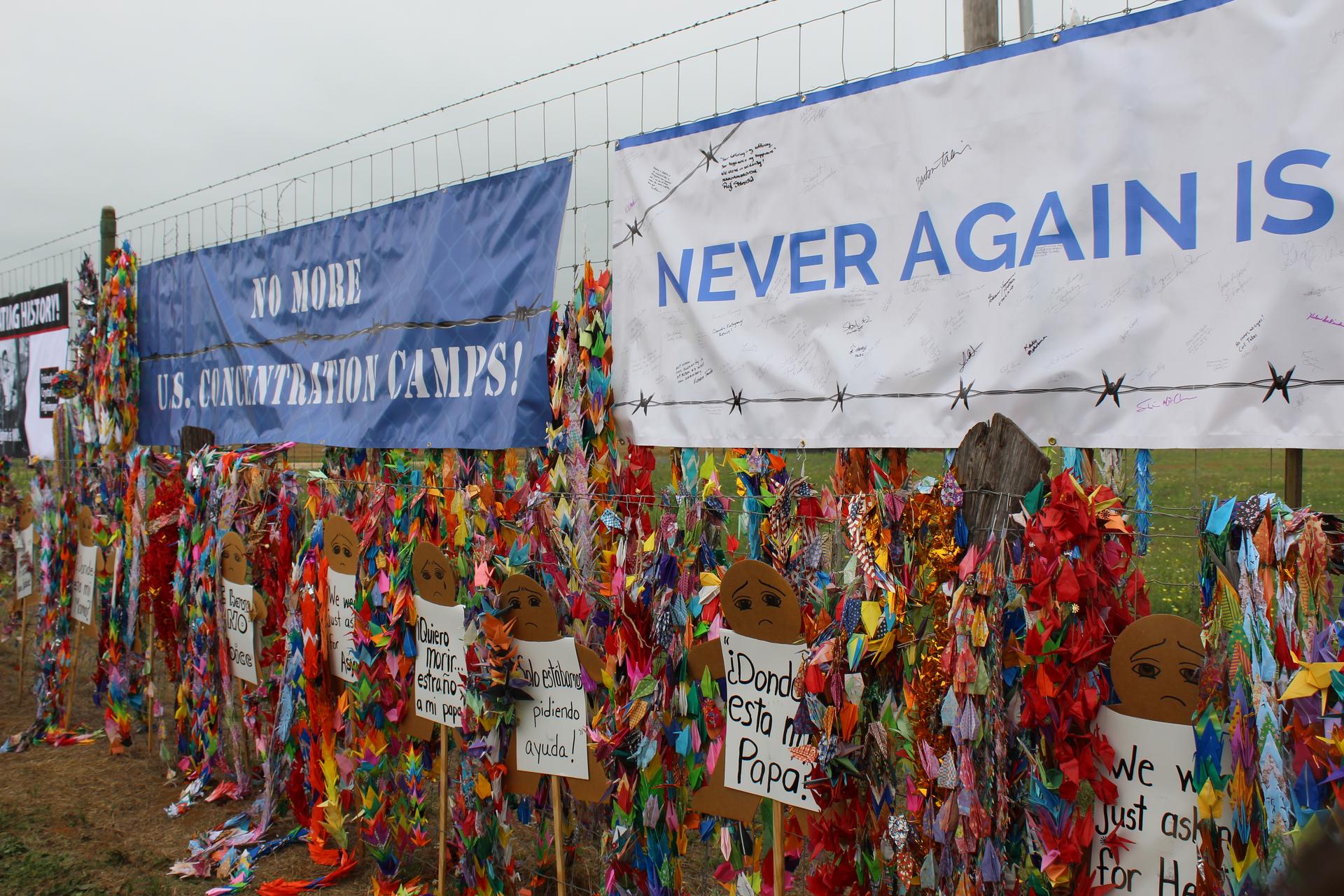 A fence strung with signs and paper cranes