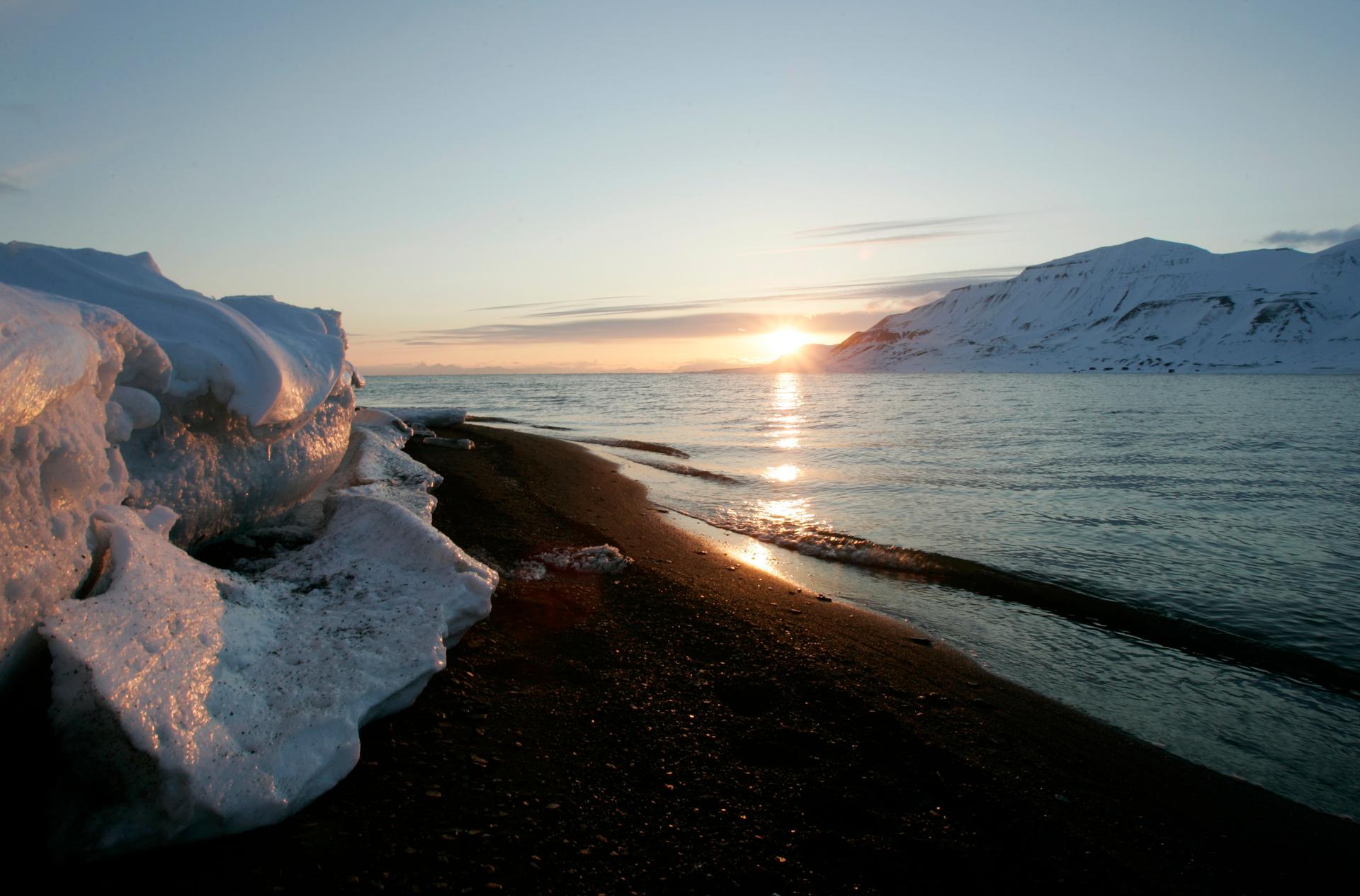 The sun sits above the horizon over melting ice in the arctic by the ocean in the arctic.