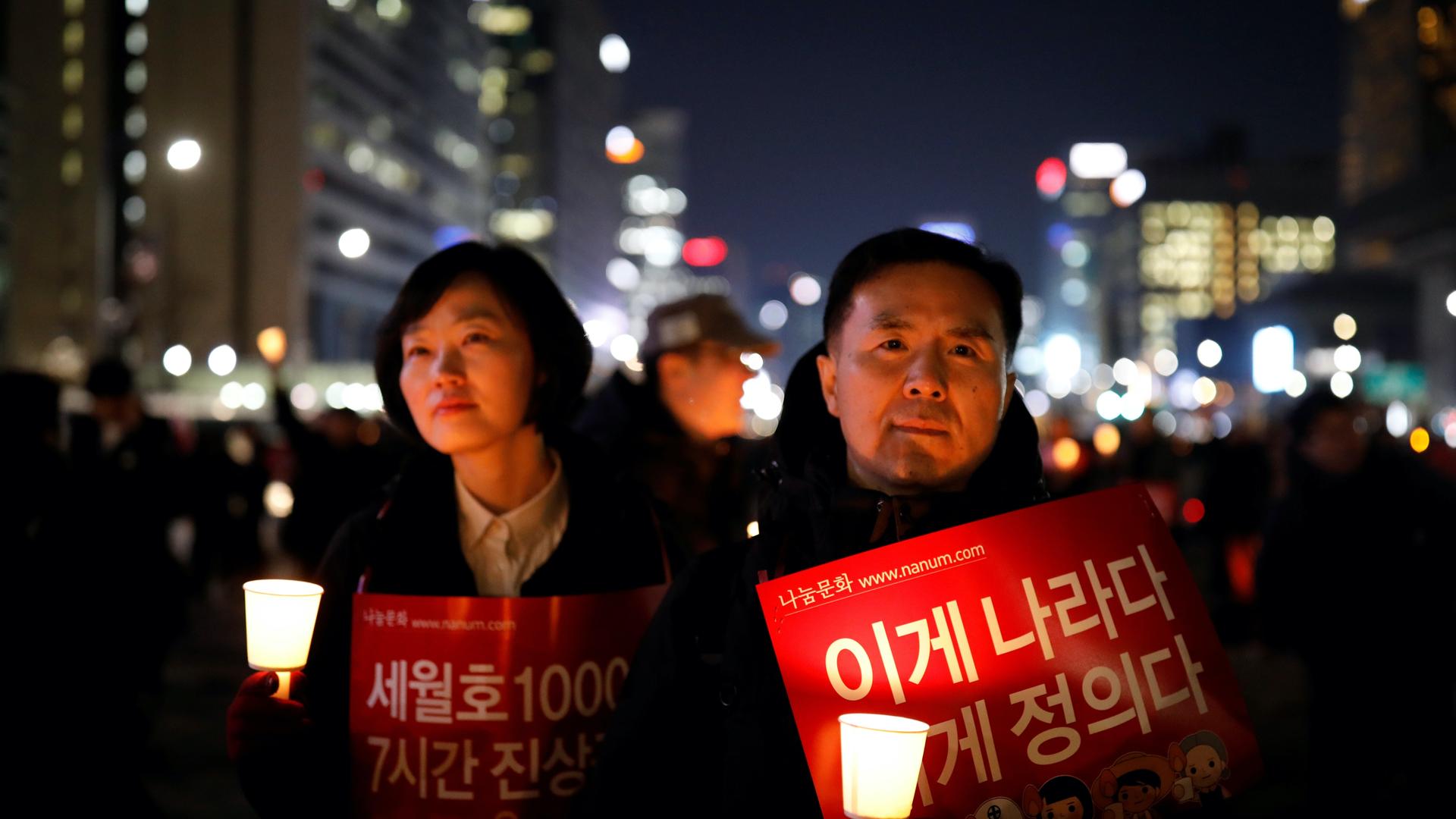 A woman and a man hold signs and candles lit up in the dark outside