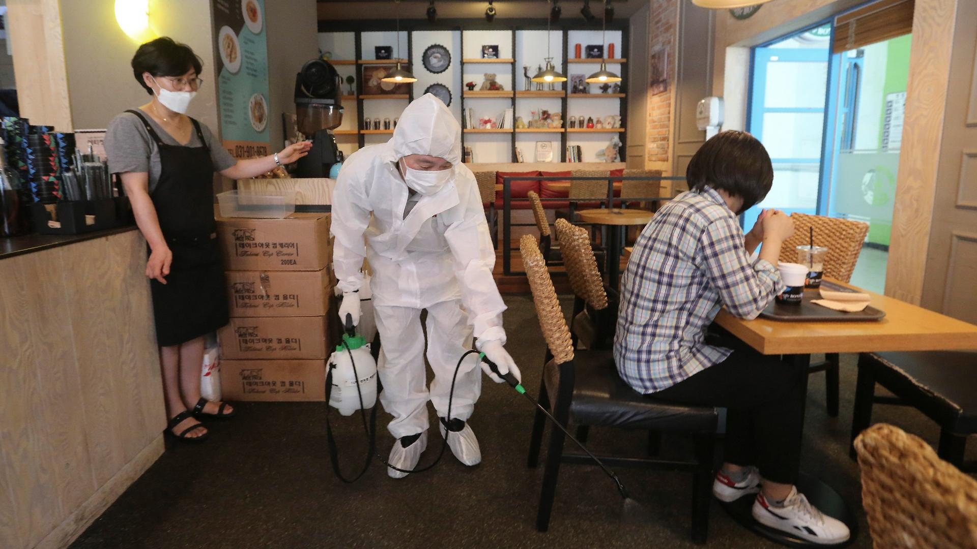 A worker dressed in white protective gear disinfects as a precaution against the coronavirus at a café in Goyang, South Korea, Aug. 25, 2020.  