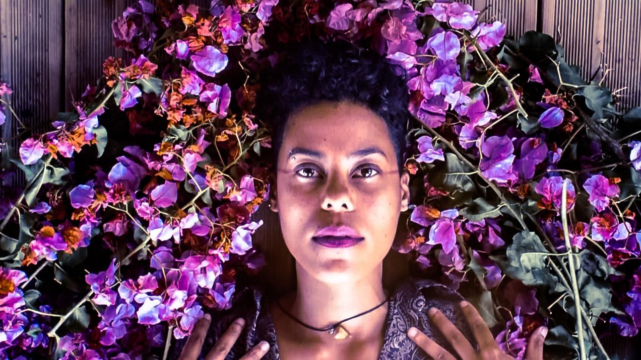 Reunion Island artist Dilo surrounded by pink and magenta flowers around her head.