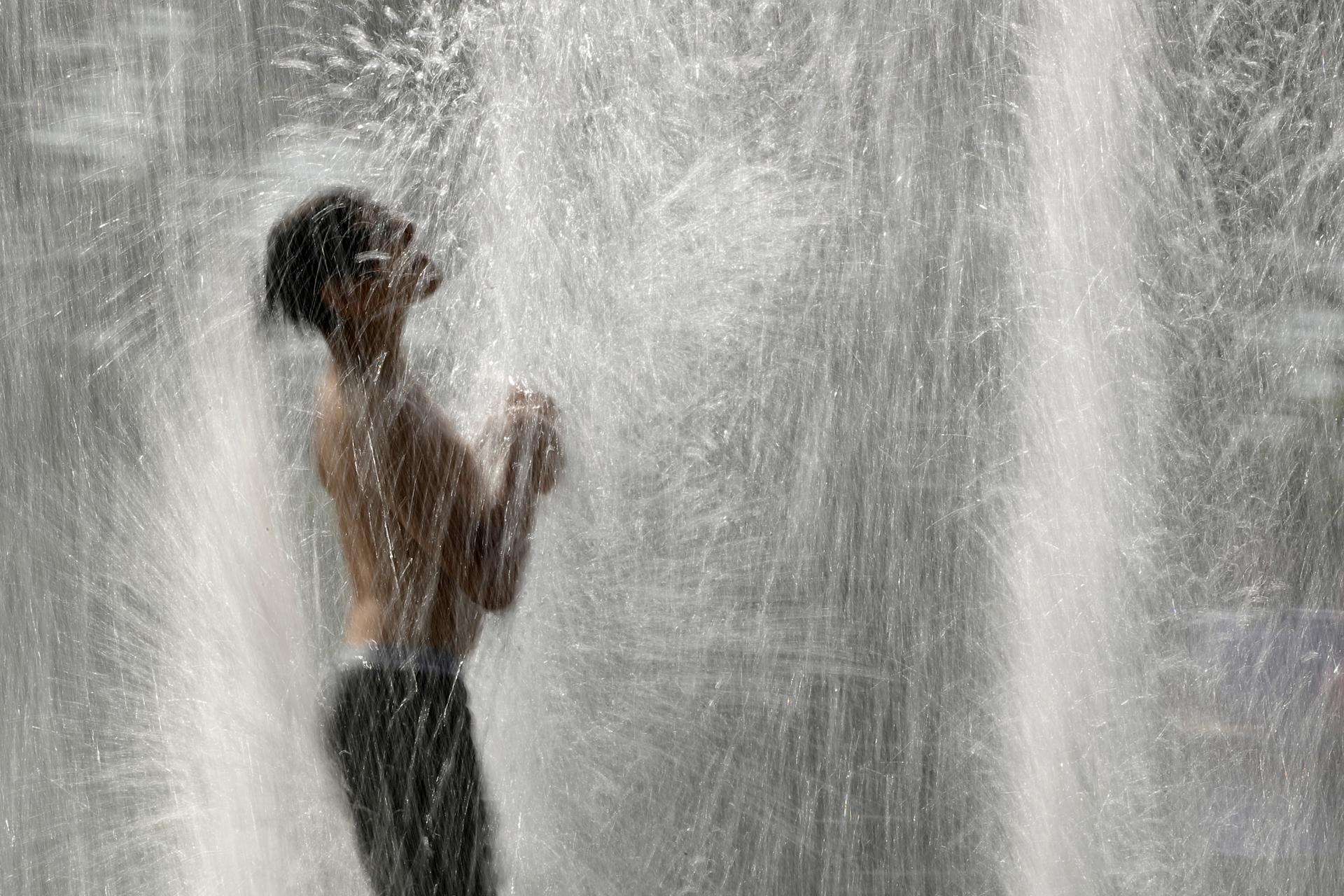 A boy plays in a fountain to cool off as temperatures approach 100 degrees Fahrenheit, July 18, 2019, in Kansas City, Missouri. 