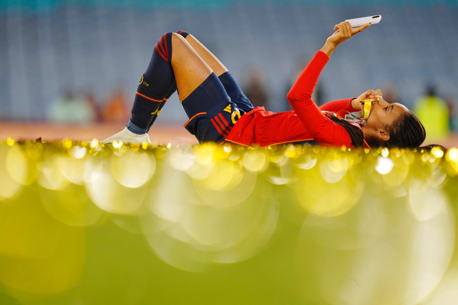 Woman eating in grass in a soccer uniform kissing a medal