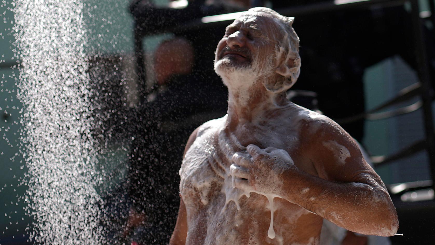 A man takes a shower as policemen patrol during an operation in Rio de Janeiro's Mare slums complex on March 30, 2014.