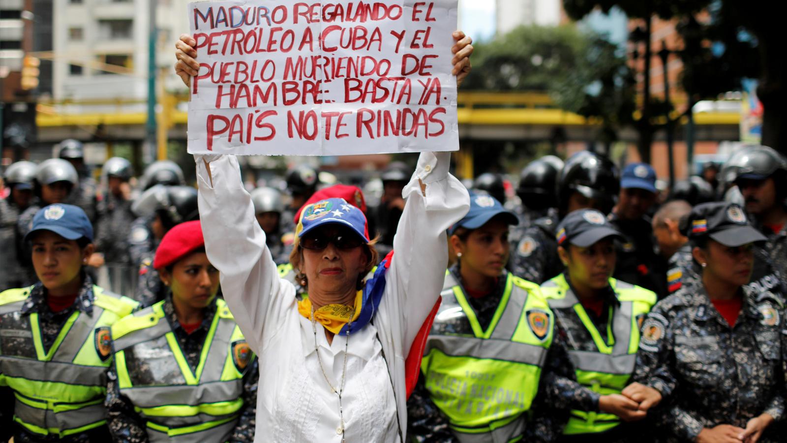 A woman holds a protest sign in Spanish.