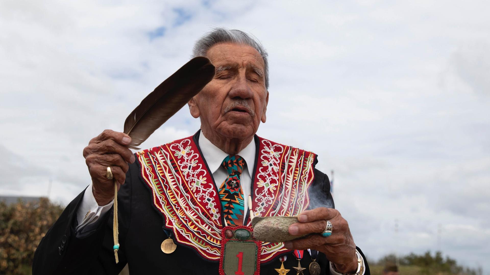 A Native American elder performs a ritual ceremony using a feather.