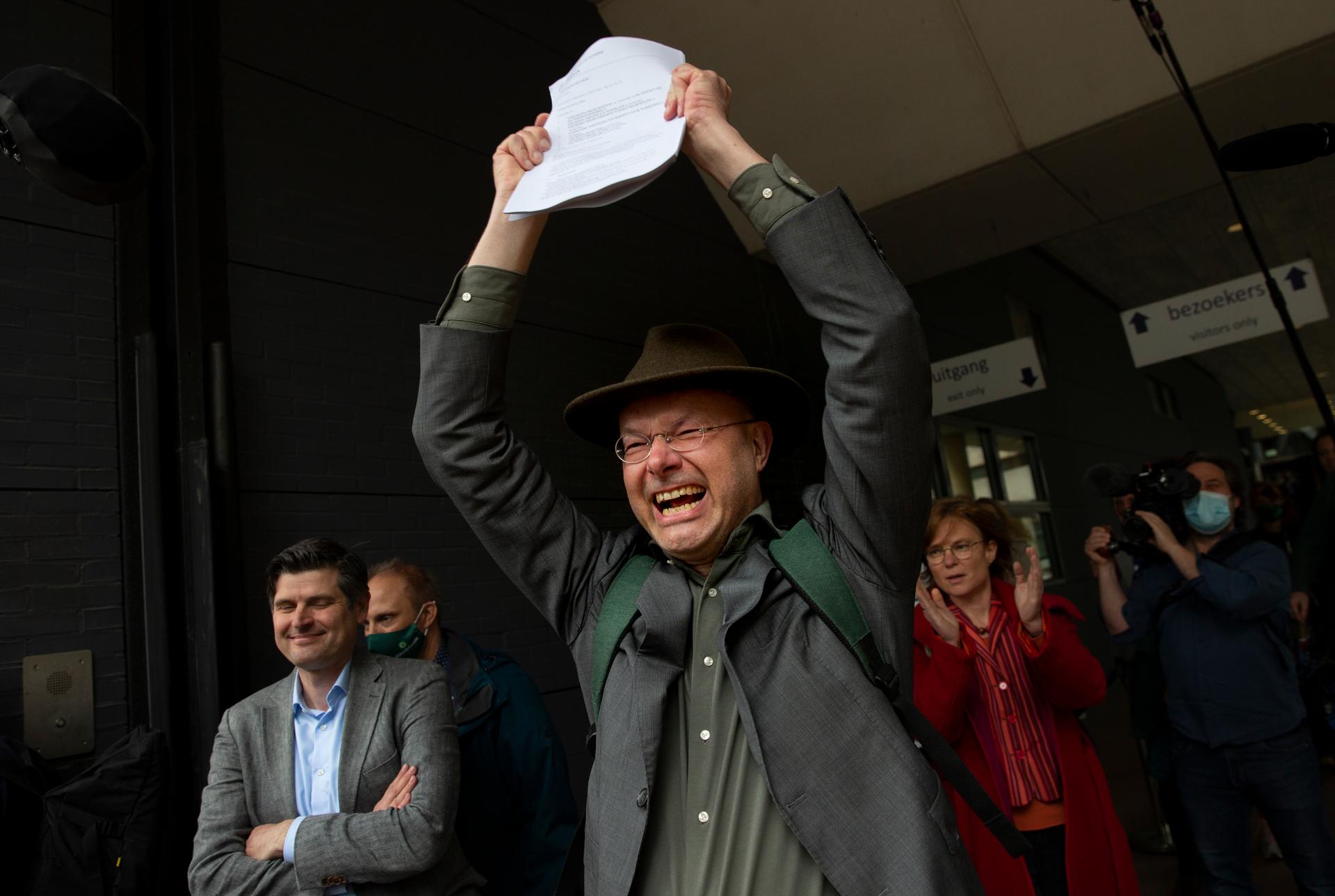 A man victoriously holds up a piece of paper and smiles as other people around him also smile