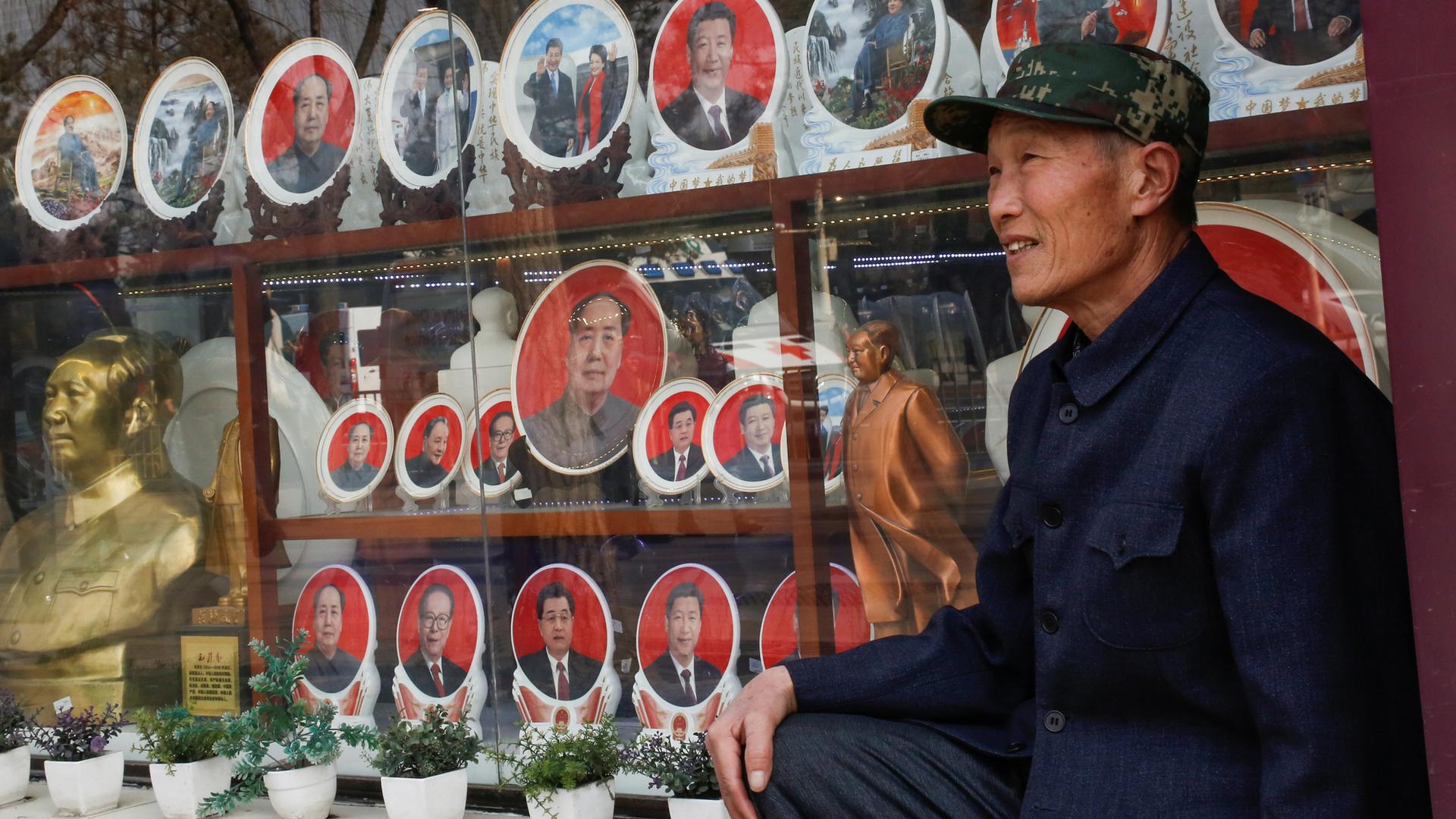 A man poses for pictures in front of souvenir plates featuring portraits of former and current Chinese leaders including President Xi Jinping and the late Chairman Mao Zedong in Tiananmen Square in Beijing, Feb. 26, 2018.