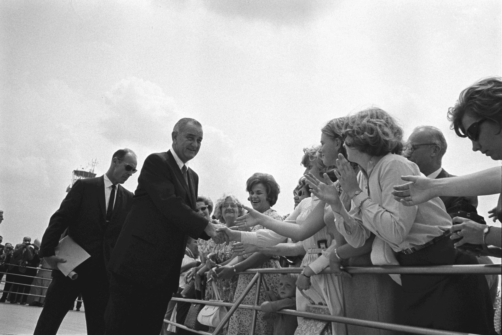 President Lyndon B. Johnson greets crowds, USSS Agent Rufus Youngblood is behind him.