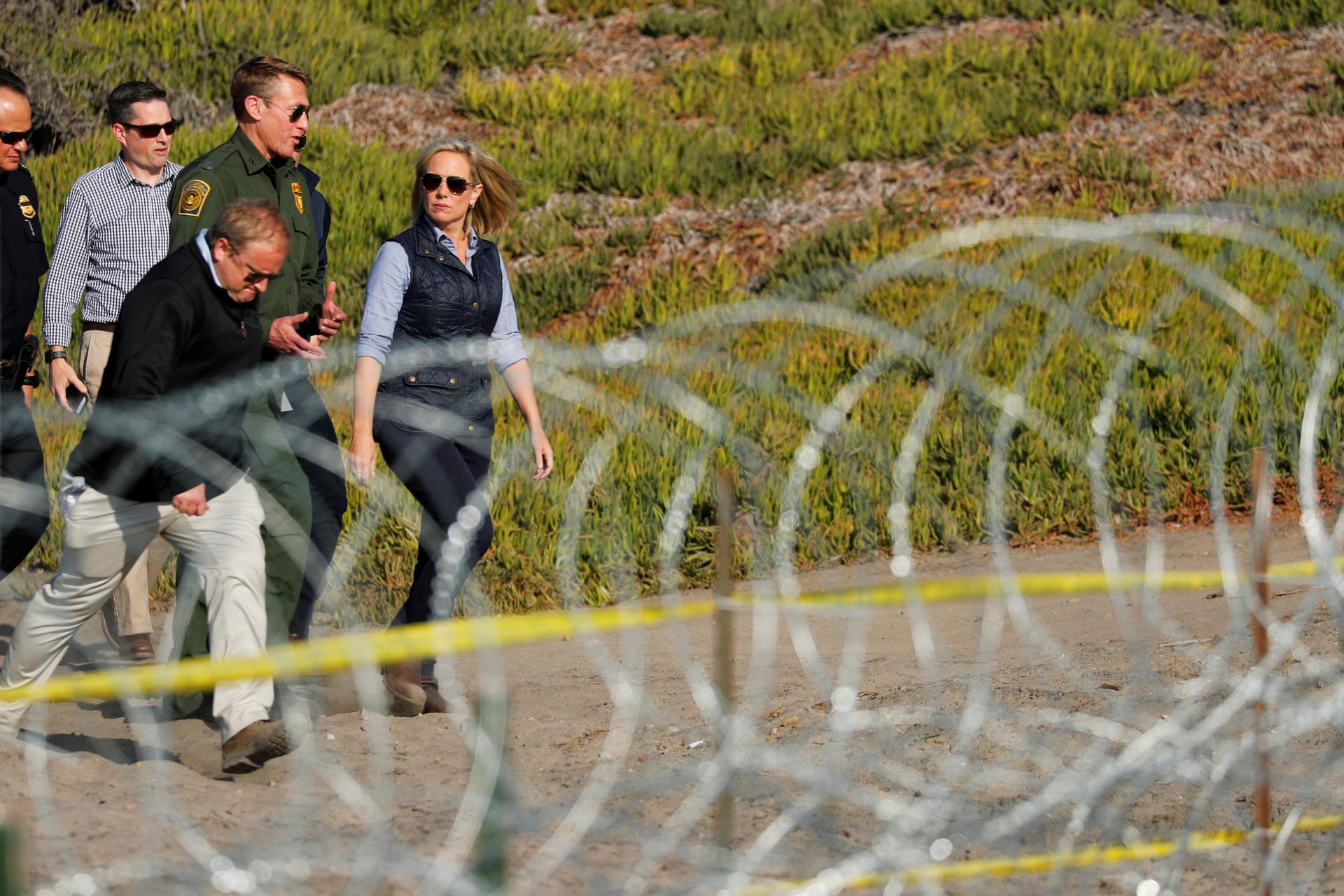 A woman and three men walk next to a fence with razor wire.