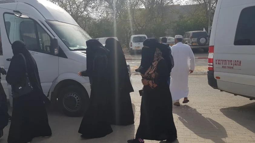 Women wearing black gowns and face veils walk near white vans