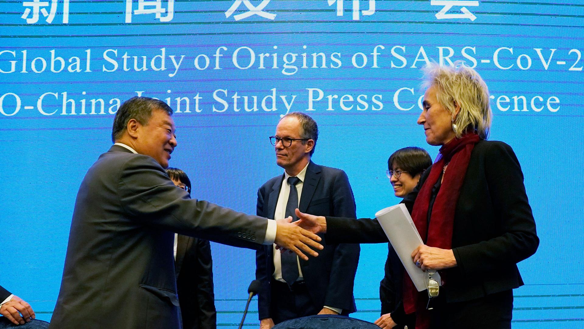 Marion Koopmans (R)is shown holding a folded white paper and reaching out to shake the hand of Liang Wannian.