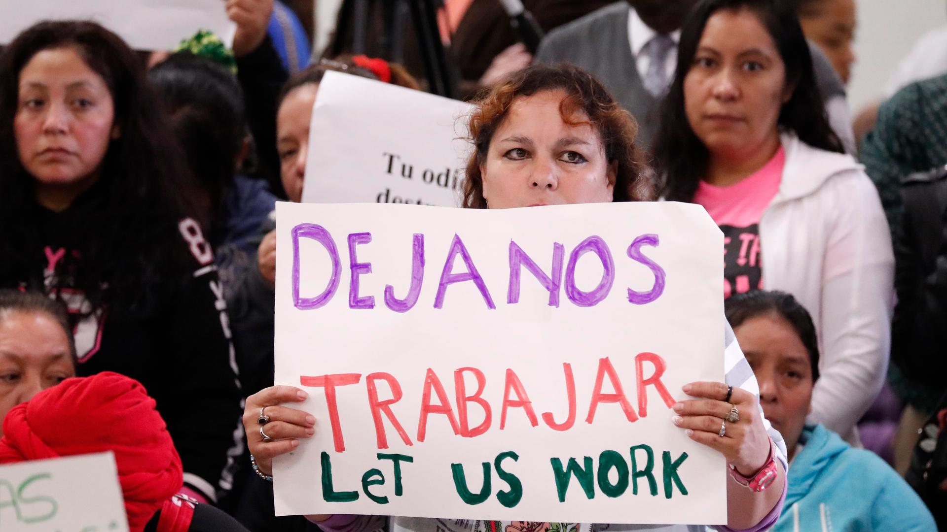 An attendee at the House Homeland Security Committee field hearing at Tougaloo College in Jackson, Mississippi, holds a sign written in English and Spanish, stating "Let us work," Thursday, Nov. 7, 2019. 
