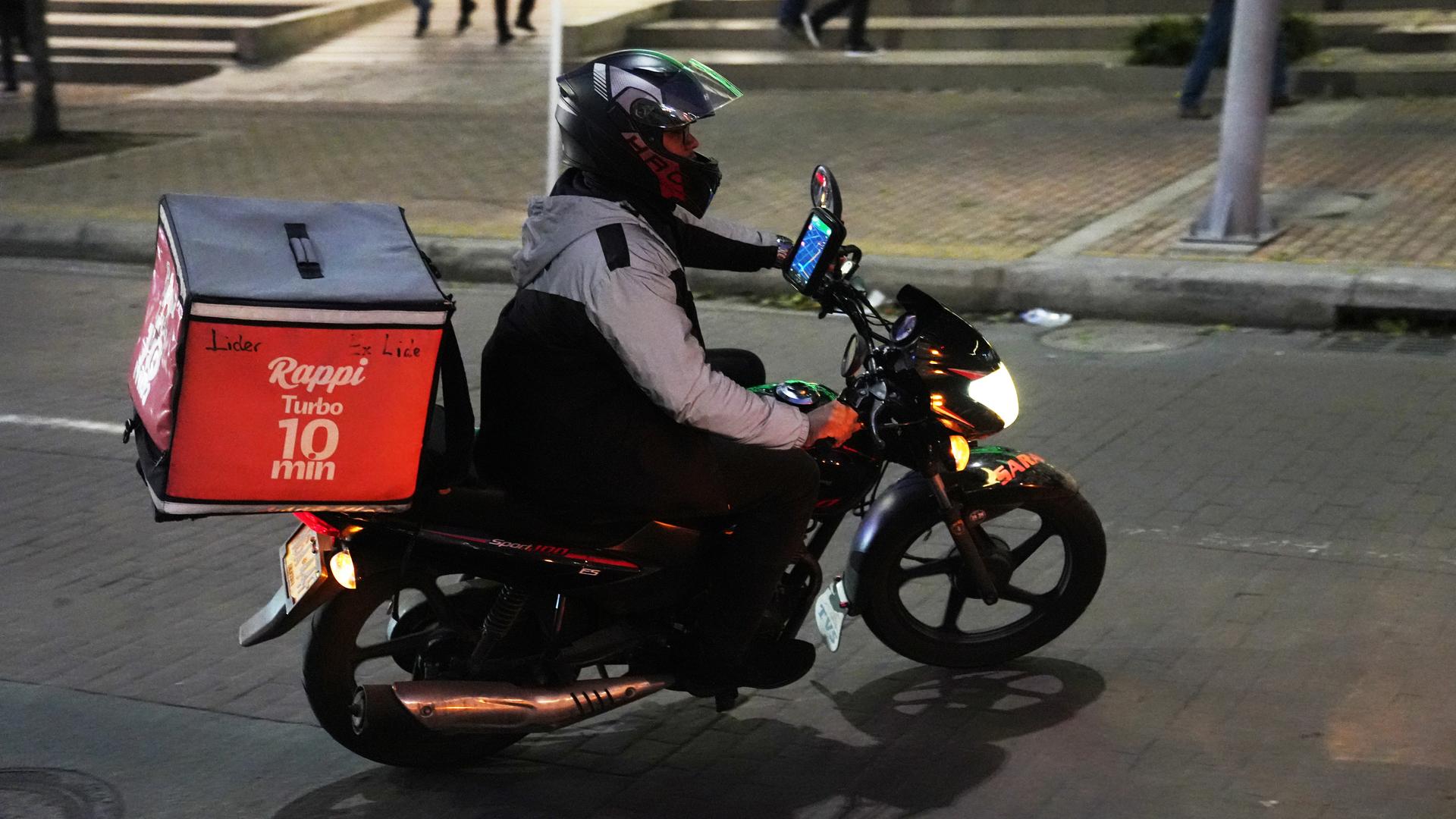A fully-covered man riding a motorbike in the street at night