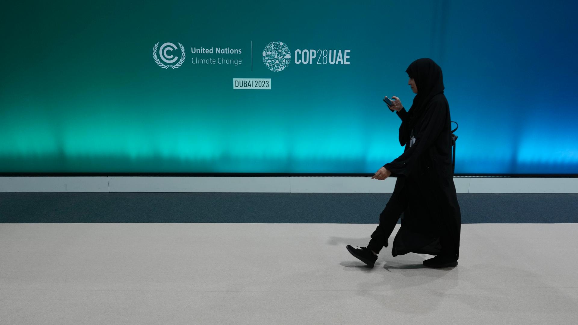 A person in all black walks past a logo at the media center ahead of the COP28 U.N. Climate Summit.