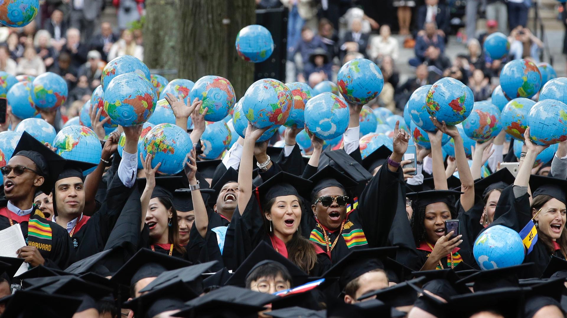 Students in black caps and gowns holding inflatable globes in the air