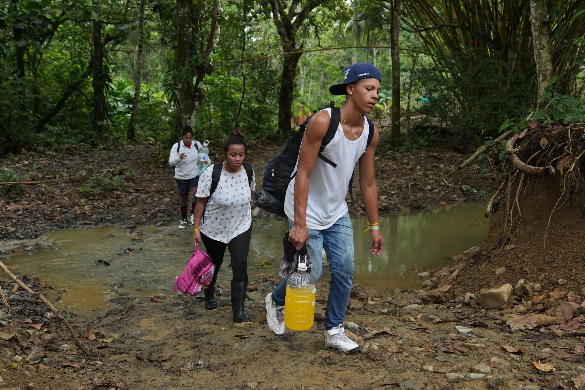 Three people cross a ravine as they walk through a forest with water bottles and backpacks.